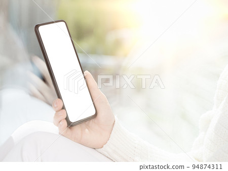 Cellphone mockup. Girl sits by window and uses cell phone, looks at smartphone, reads, shop, communicates with friends in messenger. bright light image Cellphone mockup. Girl sits by window and uses cell phone, looks at smartphone, reads, shop, communicates with friends in messenger. bright light image 94874311