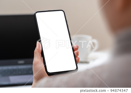 Cropped shot of businesswoman looking at blank screen smartphone in modern office room. Mockup cellphone. Woman hand holding mobile phone with blank screen 94874347