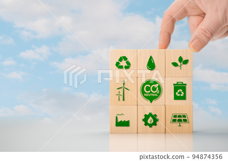 Climate neutral long term strategy. Hand put wooden cubes with green icon and green icon on blue background. Climate neutral long term strategy. Wooden cube with carbon neutral, green factory icon. 94874356