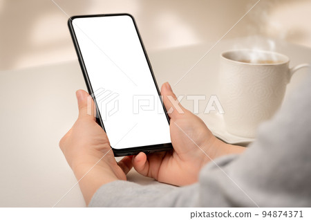 Mockup phone. Close up hand holding cellphone smartphone with blank screen in coffee shop. Woman hand using mock up smart phone at coffee shop 94874371