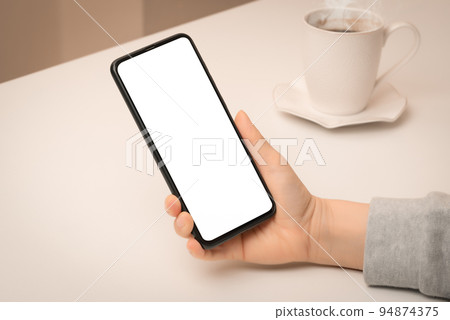 Mockup phone. Close up hand holding cellphone smartphone with blank screen in coffee shop. Woman using mock up mobile phone while sitting at cafe. Mockup phone. Close up hand holding cellphone smartphone with blank screen in coffee shop. Woman using mock up mobile phone while sitting at cafe. 94874375