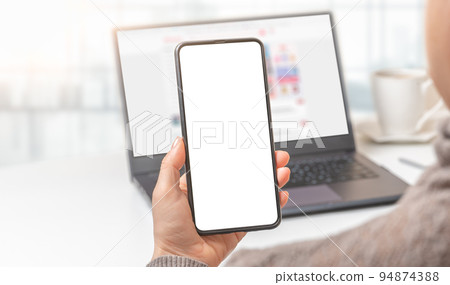 Mockup cellphone. Woman hand holding mobile phone with blank screen in modern office. hand holding smartphone with white screen in office 94874388