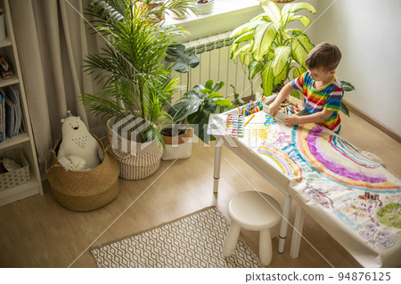 Confident cute male kid art drawing multicolored rainbow arch use paints and brush on table 94876125