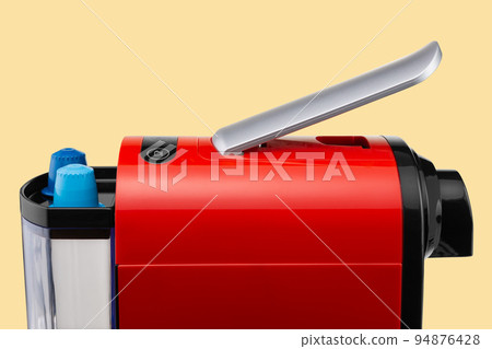 Element of a red capsule coffee machine and two capsules for making coffee, close-up, on a yellow background 94876428