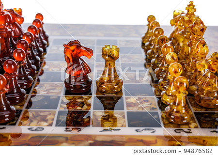 Natural amber different chess pieces figures standing on brown stone board. Close up game concept competition, Classic Gambit Tournament of confrontation. 94876582