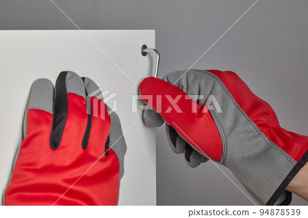Hands in red gloves twist the confirmat with a hexagon key Hands in red gloves twist the confirmat with a hexagon key 94878539