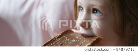 Little cute girl eating bread with chocolate pasta on top, tasty sweets Little cute girl eating bread with chocolate pasta on top, tasty sweets 94879715