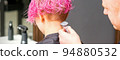 Male hairdresser shaves neck of a young caucasian woman with a short pink hairstyle by electric shaver in a hairdresser salon, close up 94880532