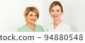 Close-up portrait of two young smiling female caucasian healthcare workers standing staring at the camera on white background 94880548