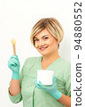 The master of sugar hair removal holds liquid yellow sugar paste, wax for depilation with the jar on a wooden stick on a white background 94880552