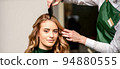 Hairdresser combing long hair of young caucasian woman looking at the camera and smiling in beauty salon 94880555