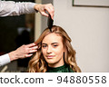 Hairdresser combing long hair of young caucasian woman looking at the camera and smiling in beauty salon 94880558