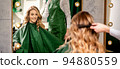 Hairdresser combing long hair of young caucasian woman looking and smiling in the mirror in beauty salon 94880559