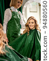 Hairdresser combing long hair of young caucasian woman looking and smiling in the mirror in beauty salon 94880560