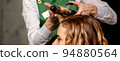 The female hairdresser is curling hair for a brown-haired young caucasian woman in a beauty salon 94880564