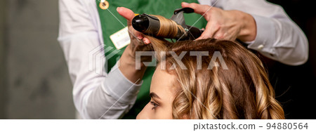 The female hairdresser is curling hair for a brown-haired young caucasian woman in a beauty salon 94880564