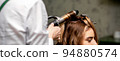 The female hairdresser is curling hair for a brown-haired young caucasian woman in a beauty salon 94880574