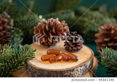 Oil capsules near fir branches and pine cones close up. Taking dietary supplements Oil capsules near fir branches and pine cones close up. Taking dietary supplements 94881346