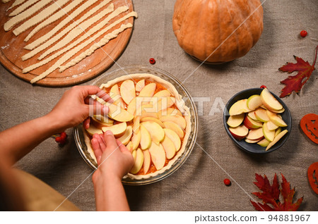Top view of housewife, chef confectioner putting slices of apples on a raw pumpkin pie, preparing homemade traditional American classic tarte with crust lattice, for Thanksgiving Day. Autumn holidays Top view of housewife, chef confectioner putting slices of apples on a raw pumpkin pie, preparing homemade traditional American classic tarte with crust lattice, for Thanksgiving Day. Autumn holidays 94881967