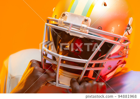 African american male american football player wearing helmet with neon orange lighting African american male american football player wearing helmet with neon orange lighting 94881968