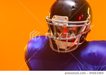 Caucasian male american football player wearing helmet with neon orange lighting Caucasian male american football player wearing helmet with neon orange lighting 94881969