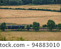 Train passing yellow grass fields in England 94883010
