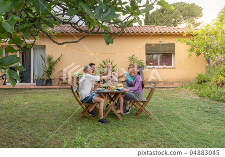 Happy friends dining and tasting together in garden in barbecue dinner party in summer. Smiling people eating at house patio. Smiles, cheerfulness concept. 94883045