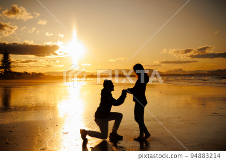 Silhouette of a man and a woman who propose at the beach at sunset 94883214