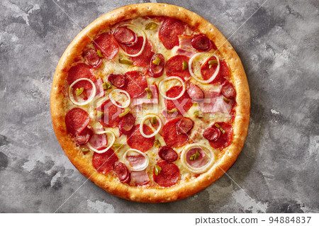 Pizza with bacon slices, salami, hunting sausages, jalapeno and onions on gray background Pizza with bacon slices, salami, hunting sausages, jalapeno and onions on gray background 94884837