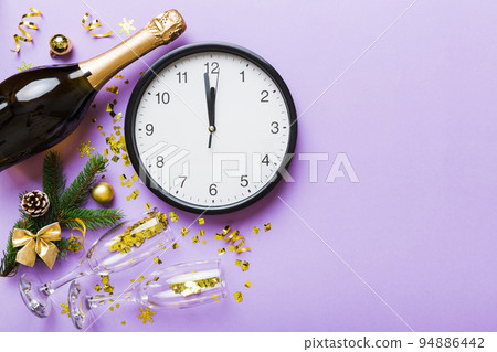 New year celebration concept with a bottle of champagne and two glasses toasting. Christmas gift box, alarm clock and fir tree branch on colored table. Top view Copy space New year celebration concept with a bottle of champagne and two glasses toasting. Christmas gift box, alarm clock and fir tree branch on colored table. Top view Copy space 94886442