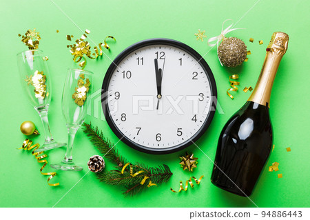 New year celebration concept with a bottle of champagne and two glasses toasting. Christmas gift box, alarm clock and fir tree branch on colored table. Top view Copy space New year celebration concept with a bottle of champagne and two glasses toasting. Christmas gift box, alarm clock and fir tree branch on colored table. Top view Copy space 94886443