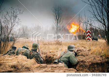 Re-enactors Dressed As World War Ii German Wehrmacht Infantry Soldiers Fighting Defensively In Trench. Defensive Position. Smokescreen. Building On Fire On Background 94886749
