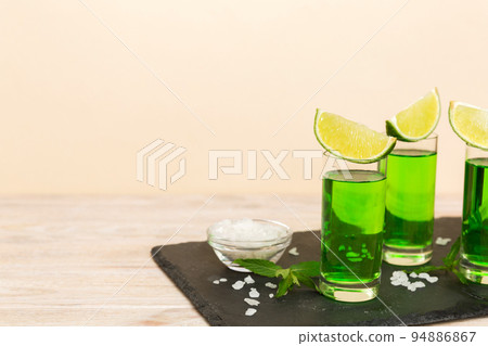 Sweet refreshing mint liqueur, with ice and mint leaves on table background, Shots with lime slice and mint flat lay Sweet refreshing mint liqueur, with ice and mint leaves on table background, Shots with lime slice and mint flat lay 94886867