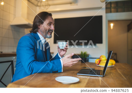 Man in blue suit having a vieo call and looking contented Man in blue suit having a vieo call and looking contented 94887625