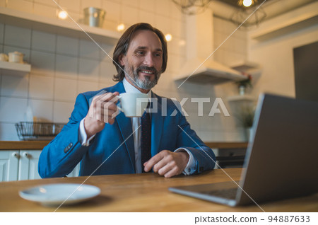 Man in blue suit having a vieo call and looking contented 94887633