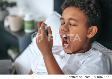 Sick boy having sore throat and spraying the remedy 94887656