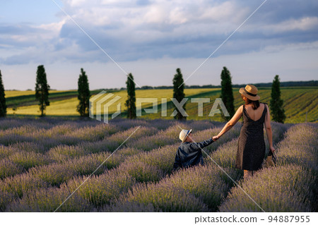 Mother and son walk hand in hand in a beautiful landscape field with lavender Mother and son walk hand in hand in a beautiful landscape field with lavender 94887955