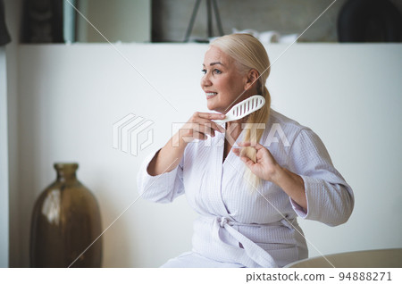 Joyful female brushing her hair seated in the bathroom Joyful female brushing her hair seated in the bathroom 94888271