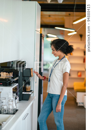 Young dark-haired woman in the office making coffee in the office canteen 94888415