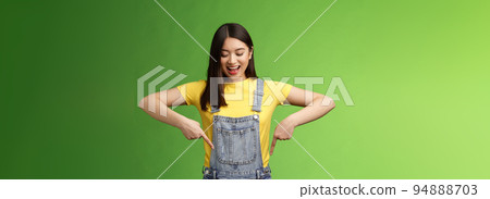 Impressed entertained cute asian girl watching pointing down interested, observe cool promo, smiling broadly, fascinated gaze bottom advertisement, take look curious thing, green background Impressed entertained cute asian girl watching pointing down interested, observe cool promo, smiling broadly, fascinated gaze bottom advertisement, take look curious thing, green background 94888703