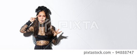 Frustrated asian woman in halloween costume arguing and complaining, scolding for something stupid, pointing finger at head and grimacing, standing over white background 94888747