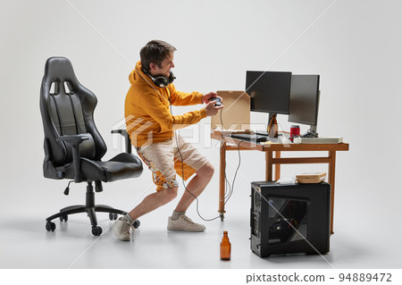Gambler. Young student sitting at home, playing computer games isolated over grey background. Hobby, studying, education, youth, remote workplace concept 94889472