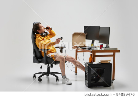 Emotional man, student sitting at home, playing computer games isolated over grey background. Hobby, studying, education, youth, remote workplace concept 94889476