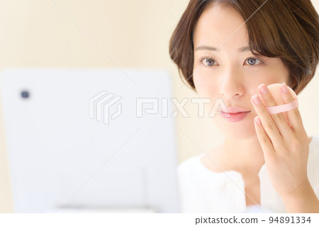 Young woman applying makeup while looking at a tablet Beauty image 94891334