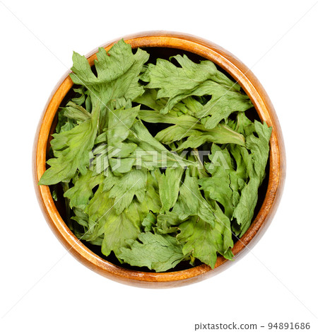 Celery, dehydrated green leaves, in a wooden bowl. Apium graveolens var. graveolens, root vegetable, primarily grown for its stalk. Leaves with strong flavor, used in soups, stews and as dried herb. 94891686