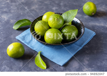 Group of fresh limes in dark blue bowl on blue napkin and on concrete background with leaves Group of fresh limes in dark blue bowl on blue napkin and on concrete background with leaves 94892847