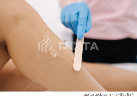 Woman beautician in blue glowes applies contact gel on the leg of a woman for laser hair removal in cosmetology studio. Close up 94893654