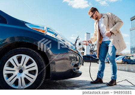 Stylish man in sunglasses inserts the charging cable into the socket of electric car 94893881