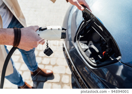 Man inserts plug of the charger into the socket of electric car close-up 94894001
