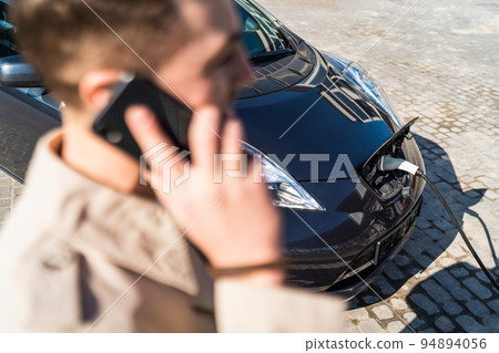 Man talks on the phone while his car is charging at the station 94894056